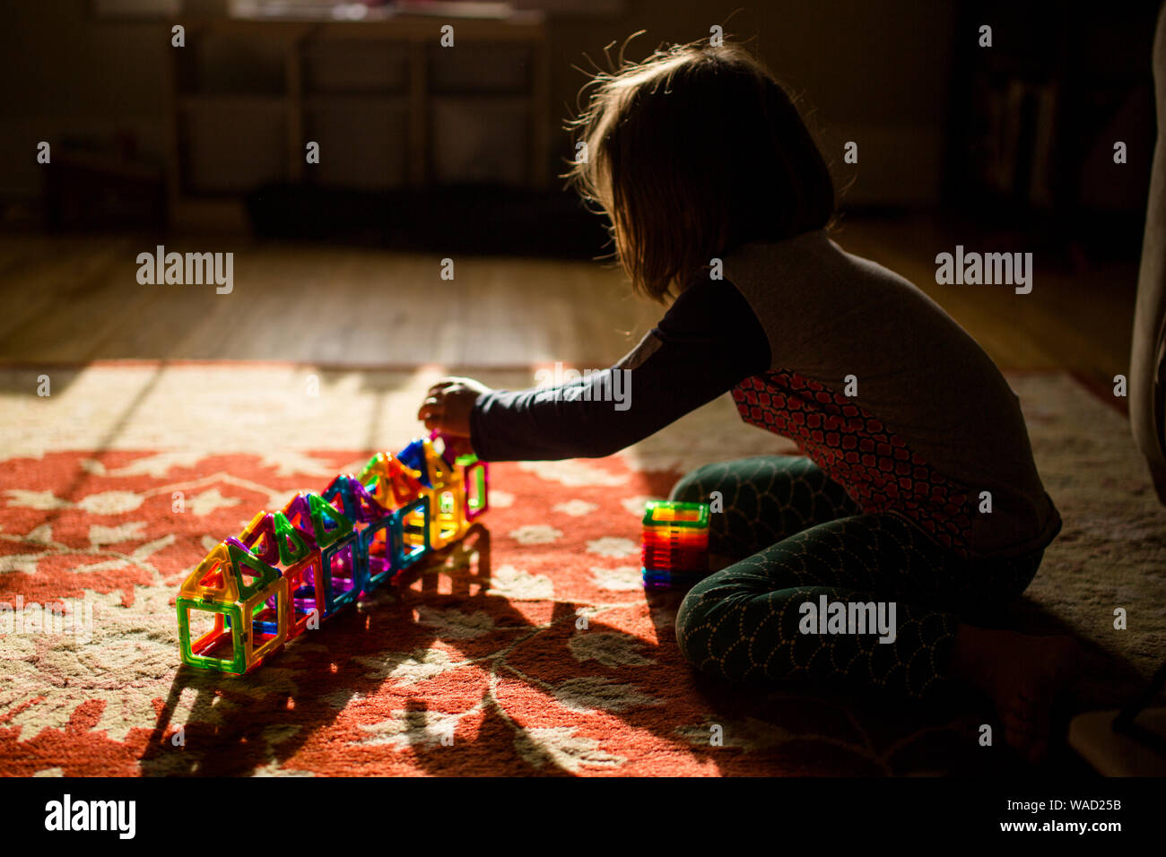 A child sits on the floor in golden morning light building with tiles Stock Photo