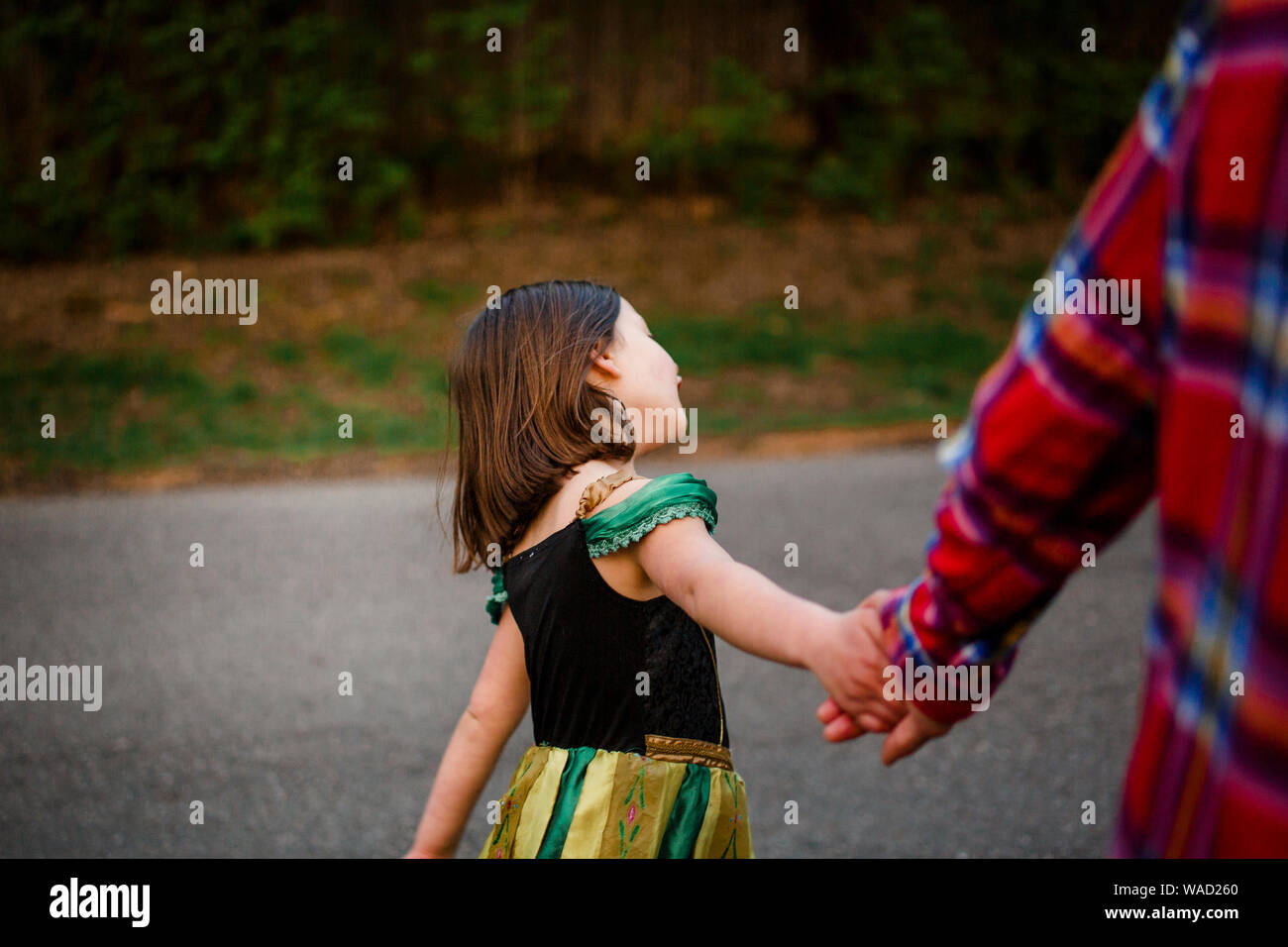 A small child in a princess costume holds her father's hands on a walk Stock Photo