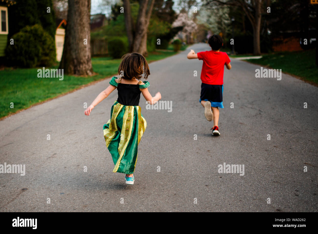 two children skip happily down a tree-lined street in springtime Stock Photo