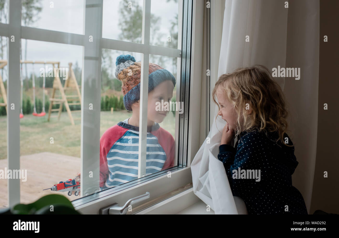 brother and sister looking through a window at each other playing Stock Photo