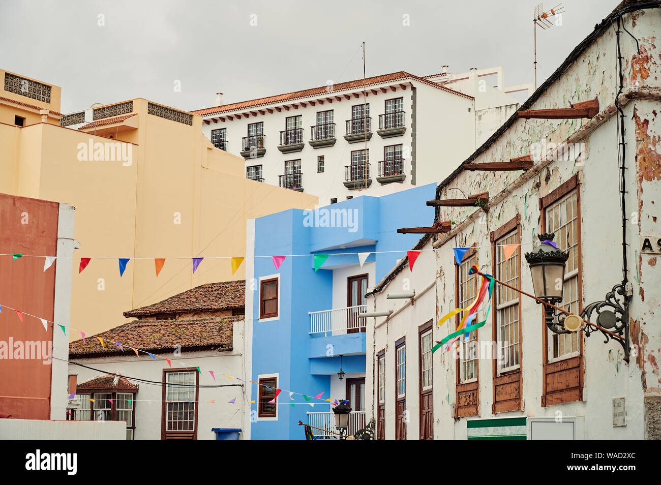 Simple exterior of colorful houses with tiled roofs and balconies on authentic street decorated with flag garlands in Tenerife, Spain Stock Photo
