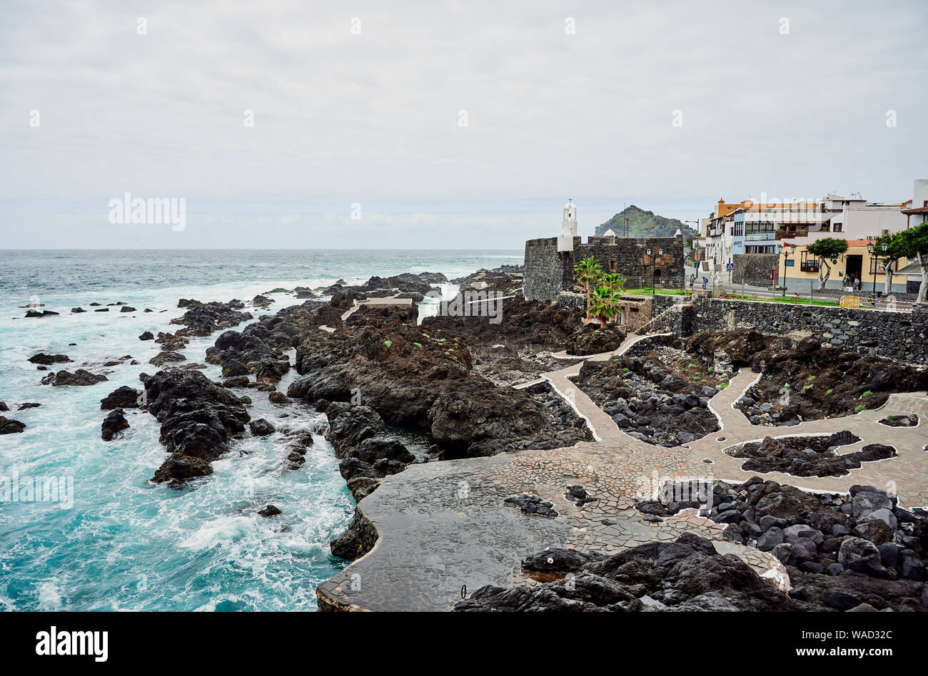 Majestic view of rocky shore with paved paths and black stones between small town and turquoise wavy ocean on nasty day, Tenerife, Spain Stock Photo