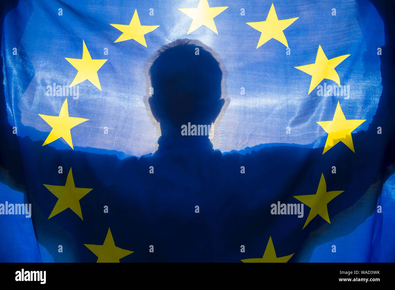 Shadow silhouette of a man holding an EU European Union flag backlit by the rising sun Stock Photo