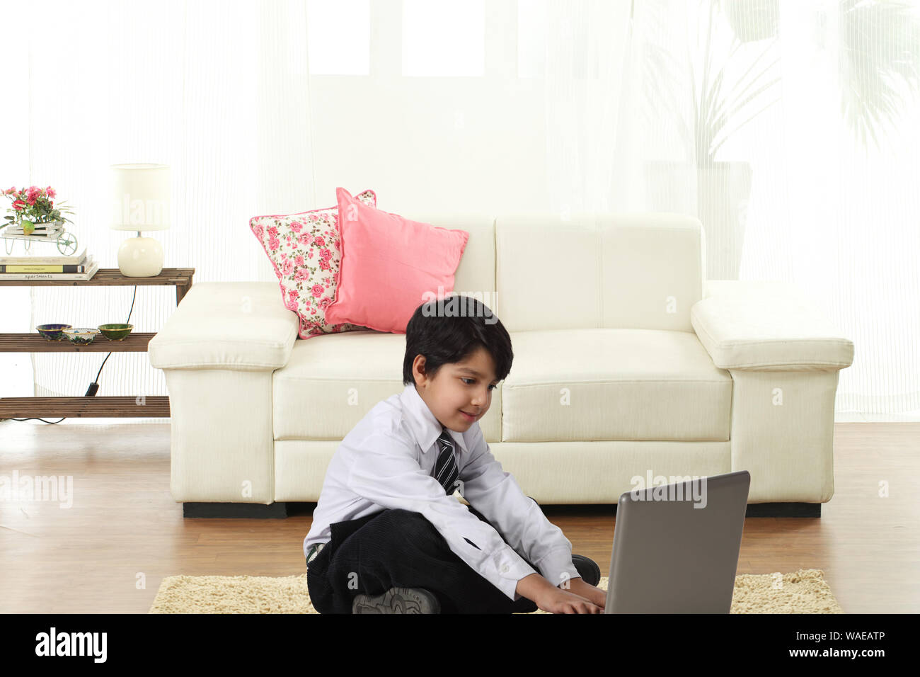 Schoolboy sitting on floor and using laptop Stock Photo