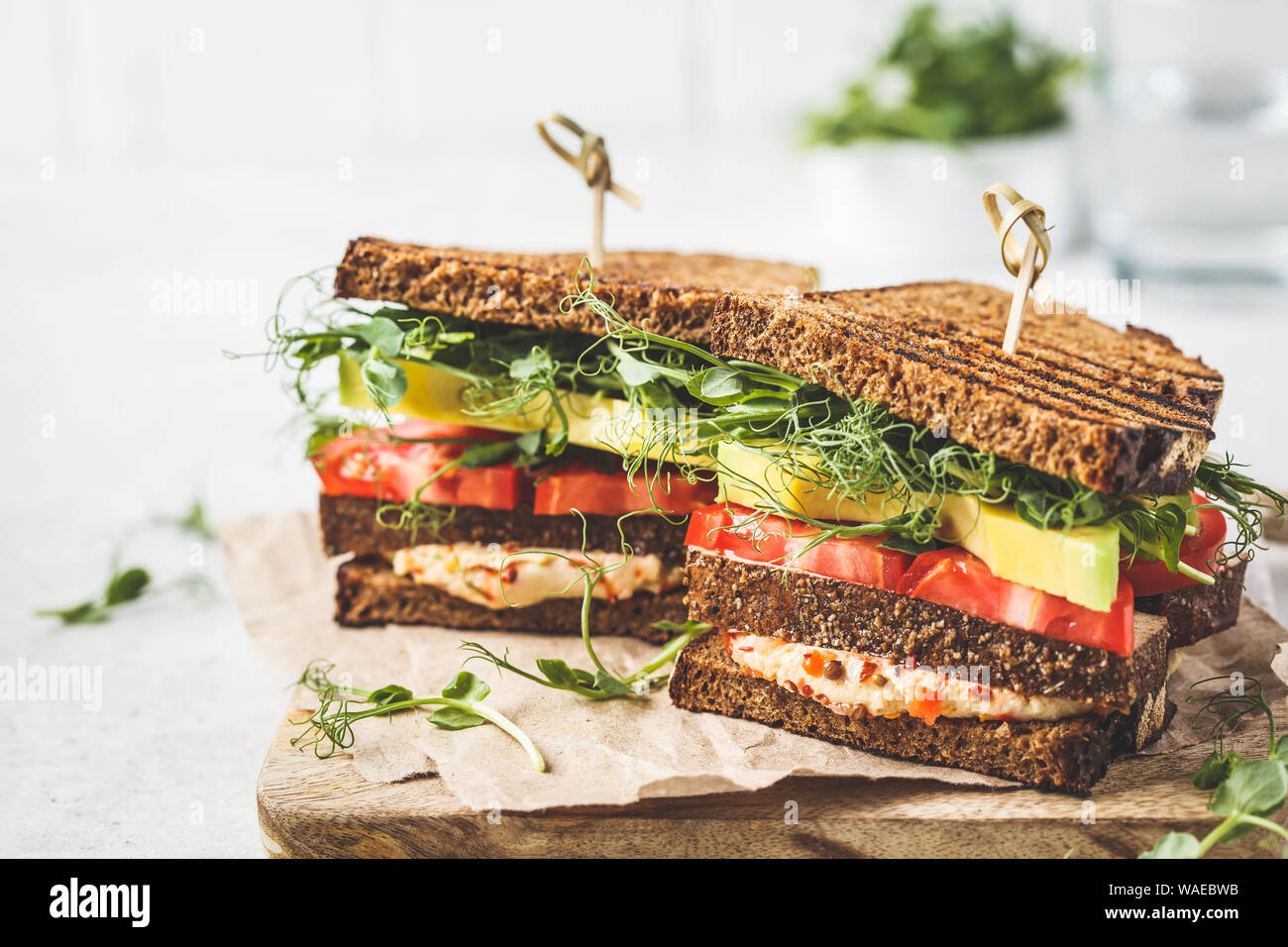 Vegan sandwich with tofu, hummus, avocado, tomato and sprouts on board