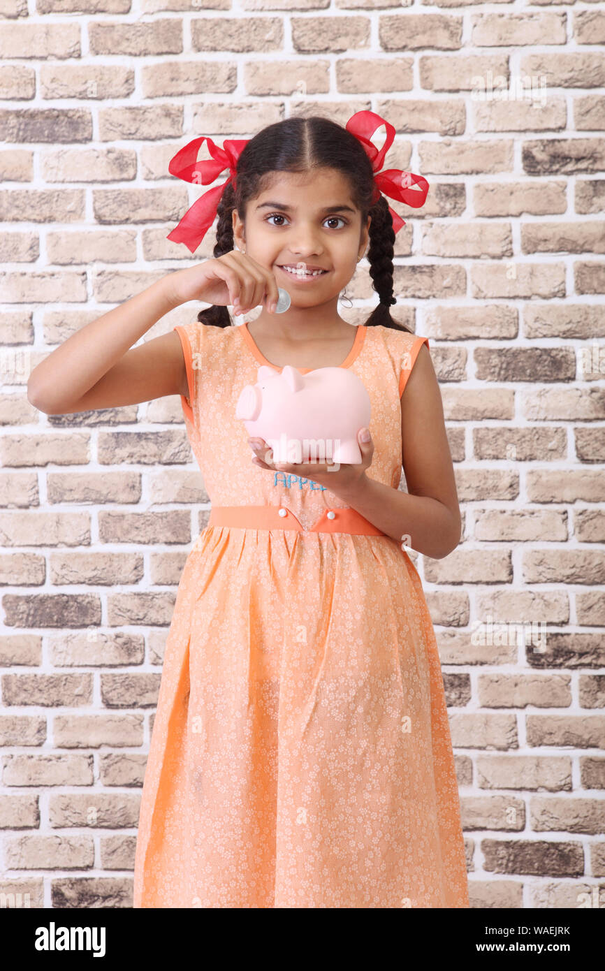 Girl inserting a coin into a piggy bank Stock Photo - Alamy