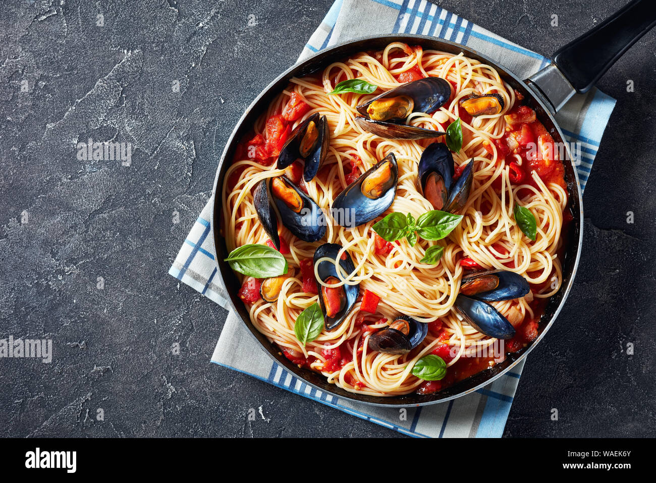 spaghetti with Mussels in a Spicy Tomato Sauce in a skillet on a concrete table, horizontal view from above, flatlay, empty space Stock Photo