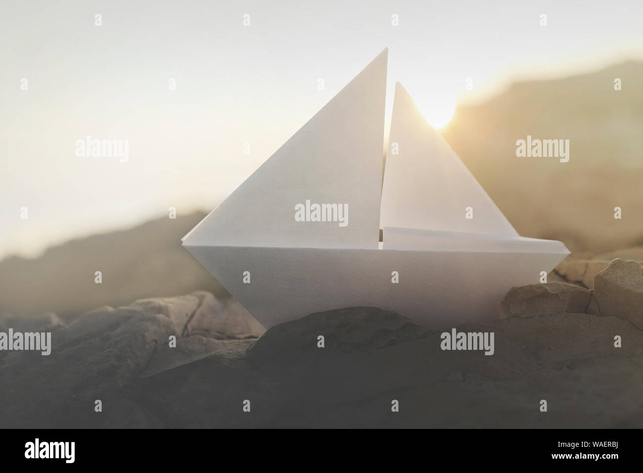 origami boat sails on the rocks illuminated by the sun Stock Photo