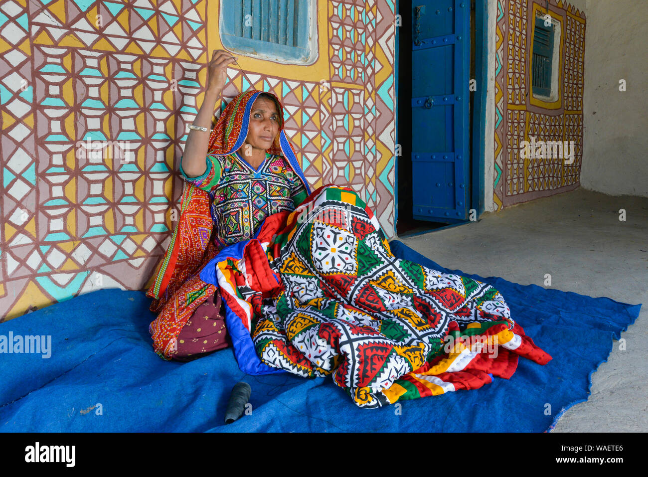 Woman in traditional cloth sewing handicraft in front of a house, Khavda tourist village, Great Rann of Kutch Desert, Gujarat, India Stock Photo