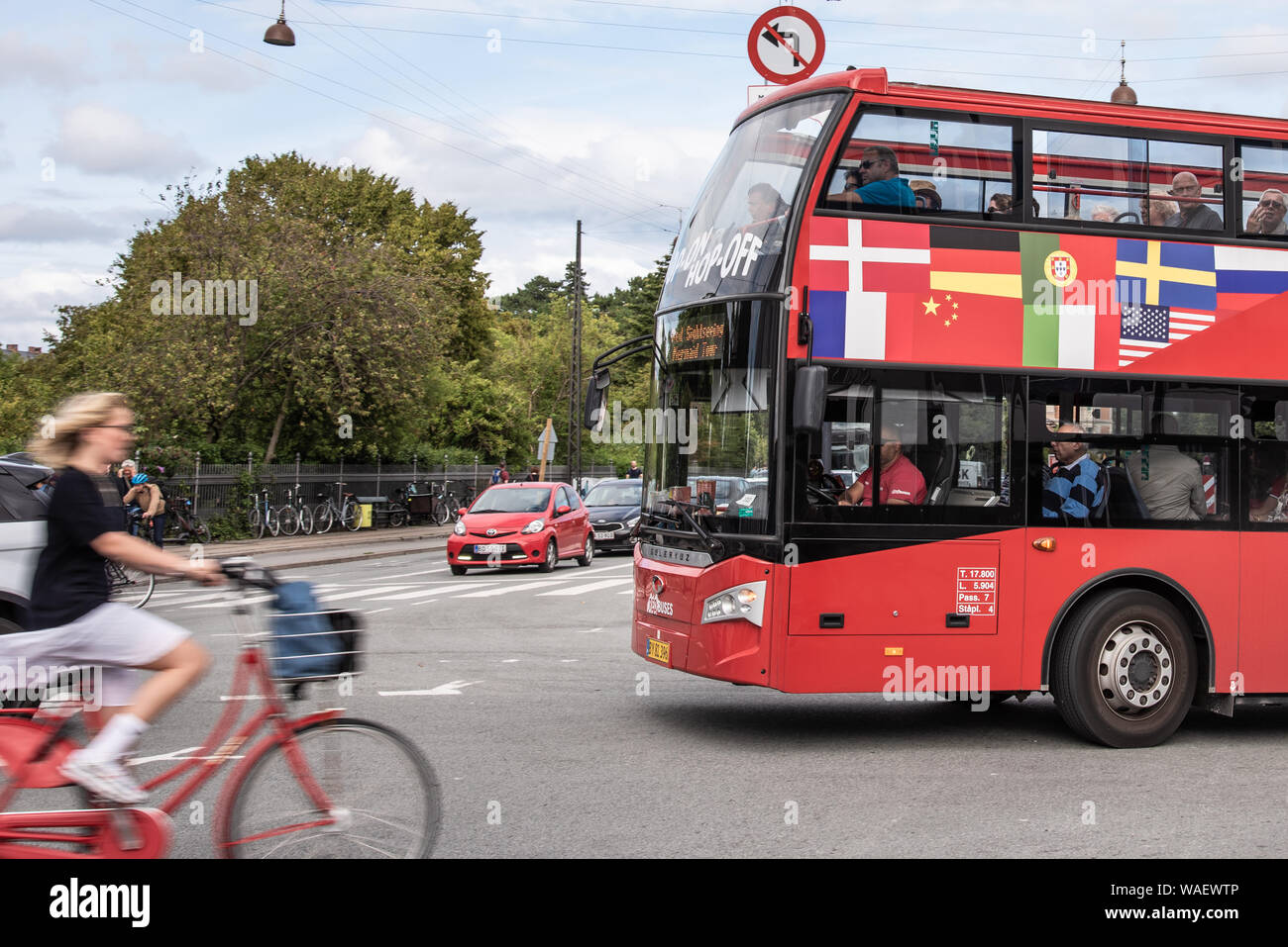 woman cycling without a helmet in front of a red hop on hop off bus in Copenhagen, August 16, 2019 Stock Photo