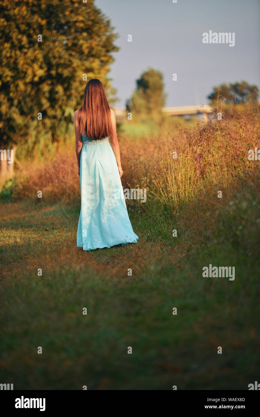 Rear View of Beautiful Young Woman in light blue frok standing in a field Stock Photo