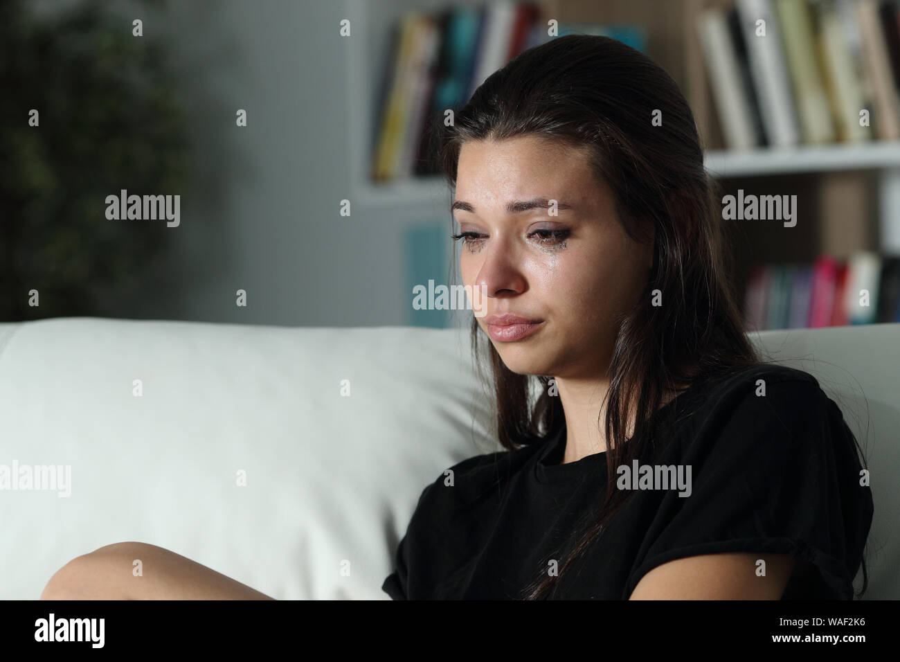 Sad girl crying looking away alone sitting on a couch in the living room at home Stock Photo