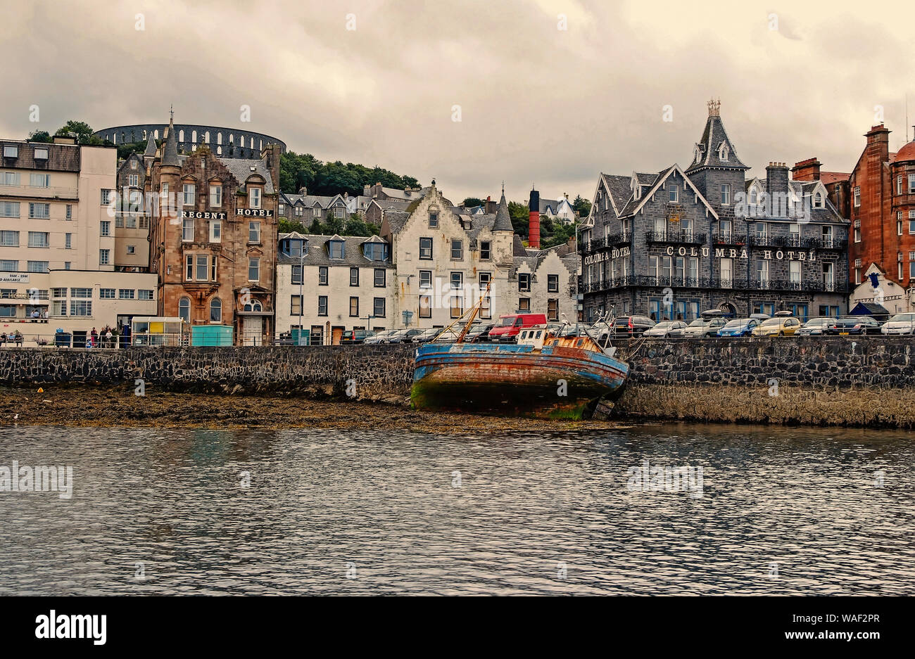 Oban, United Kingdom - February 20, 2010: bay with houses on grey sky. City architecture along sea quay. Resort town with hotels. Summer vacation on island. Travelling and wanderlust. Stock Photo