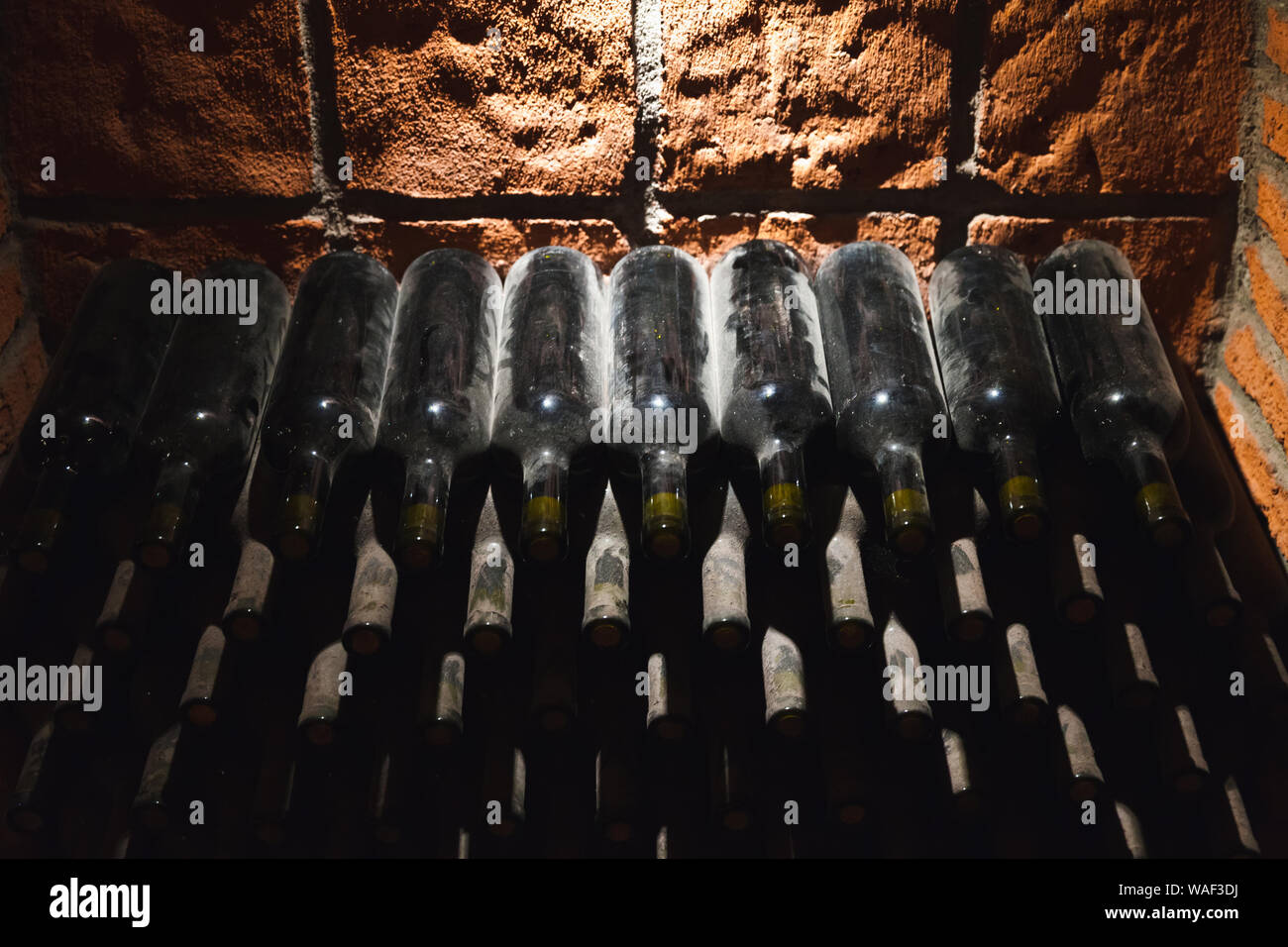 Stacked dusty bottles of wine lay in a dark wine Vault Stock Photo