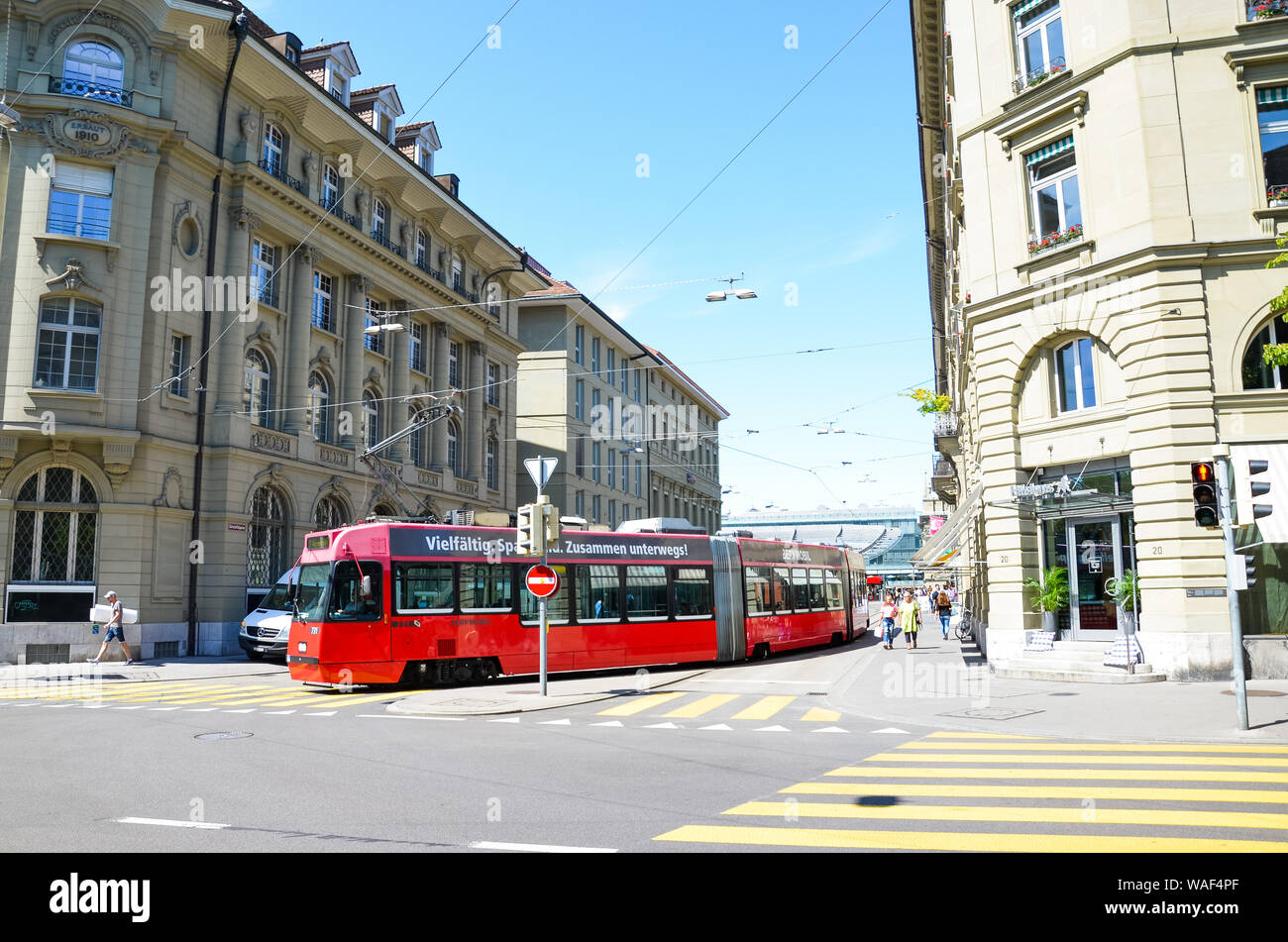 Bern, Switzerland - August 14 2019: Red tram in the city center of the Swiss capital. Red light on zebra crossing, city crossroad. Historical buildings, people walking. Sunny summer day. Stock Photo