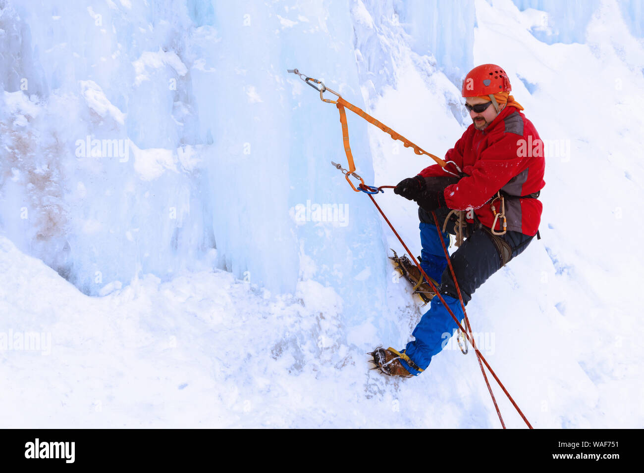 climber uses figure eight belay device on the ice wall of a glacier