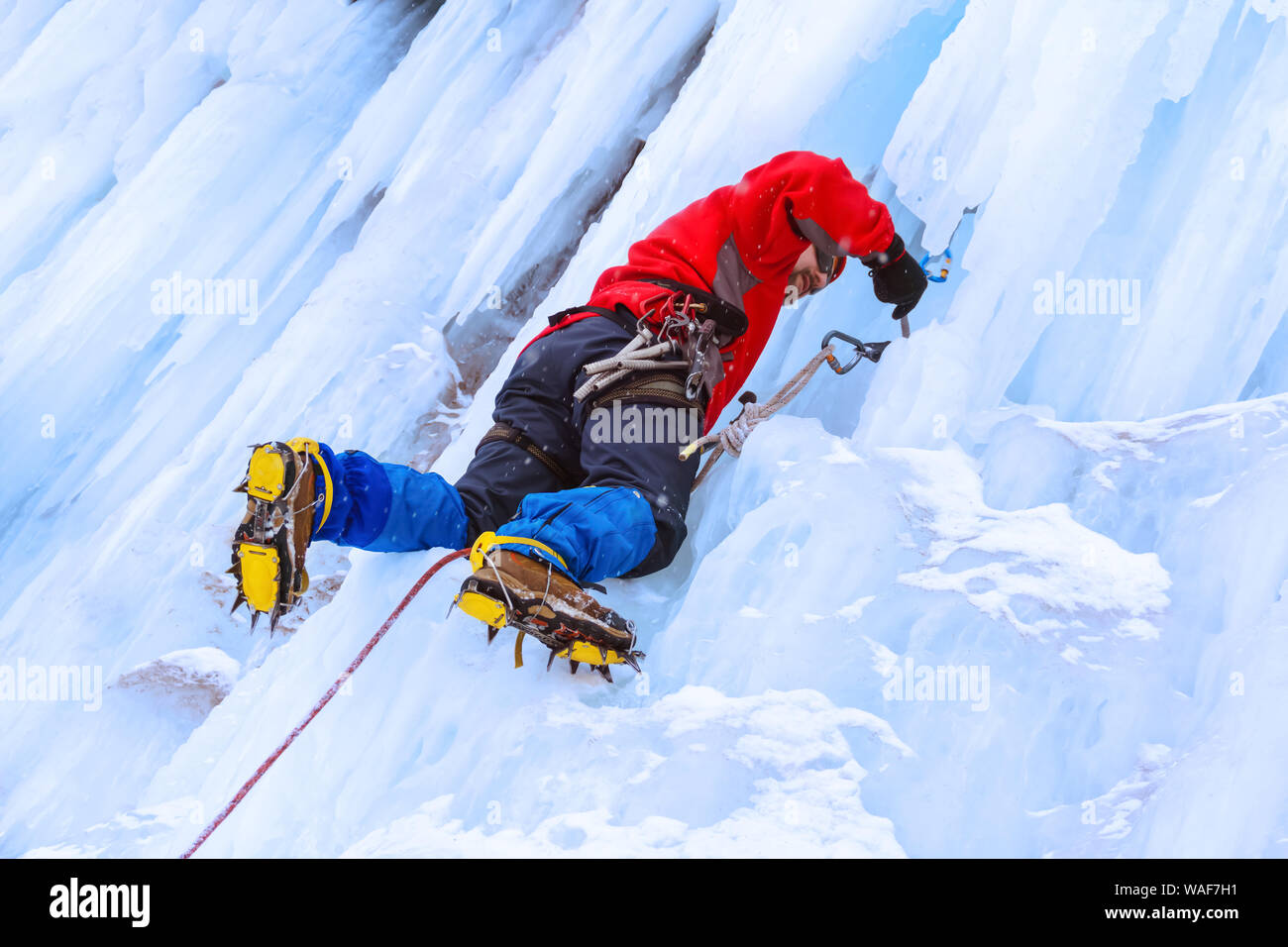 ice climber preraring running belay, screwing ice screw into glacier