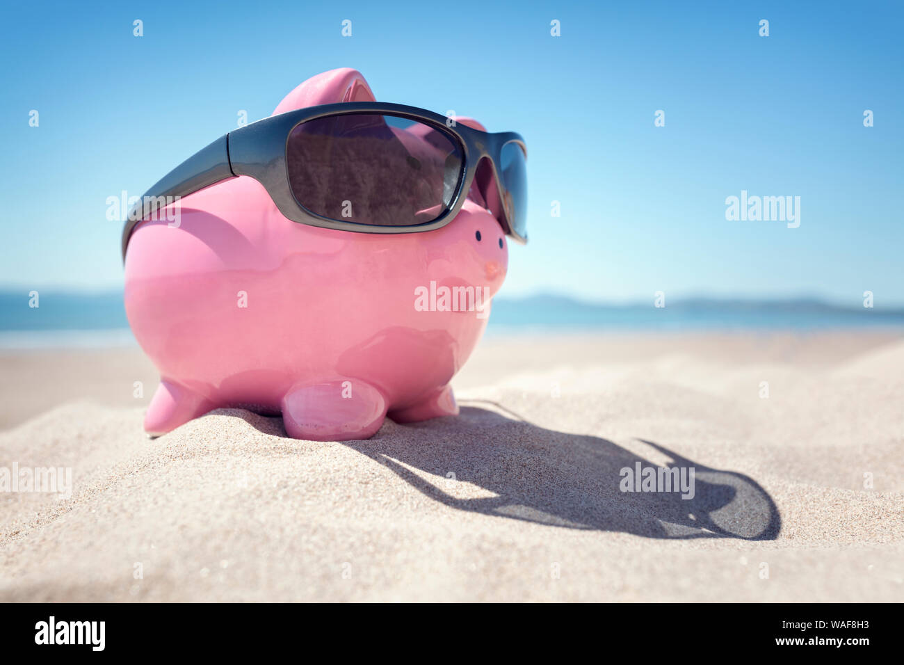 Piggy bank with sunglasses on the beach at the seaside in Summer Stock Photo