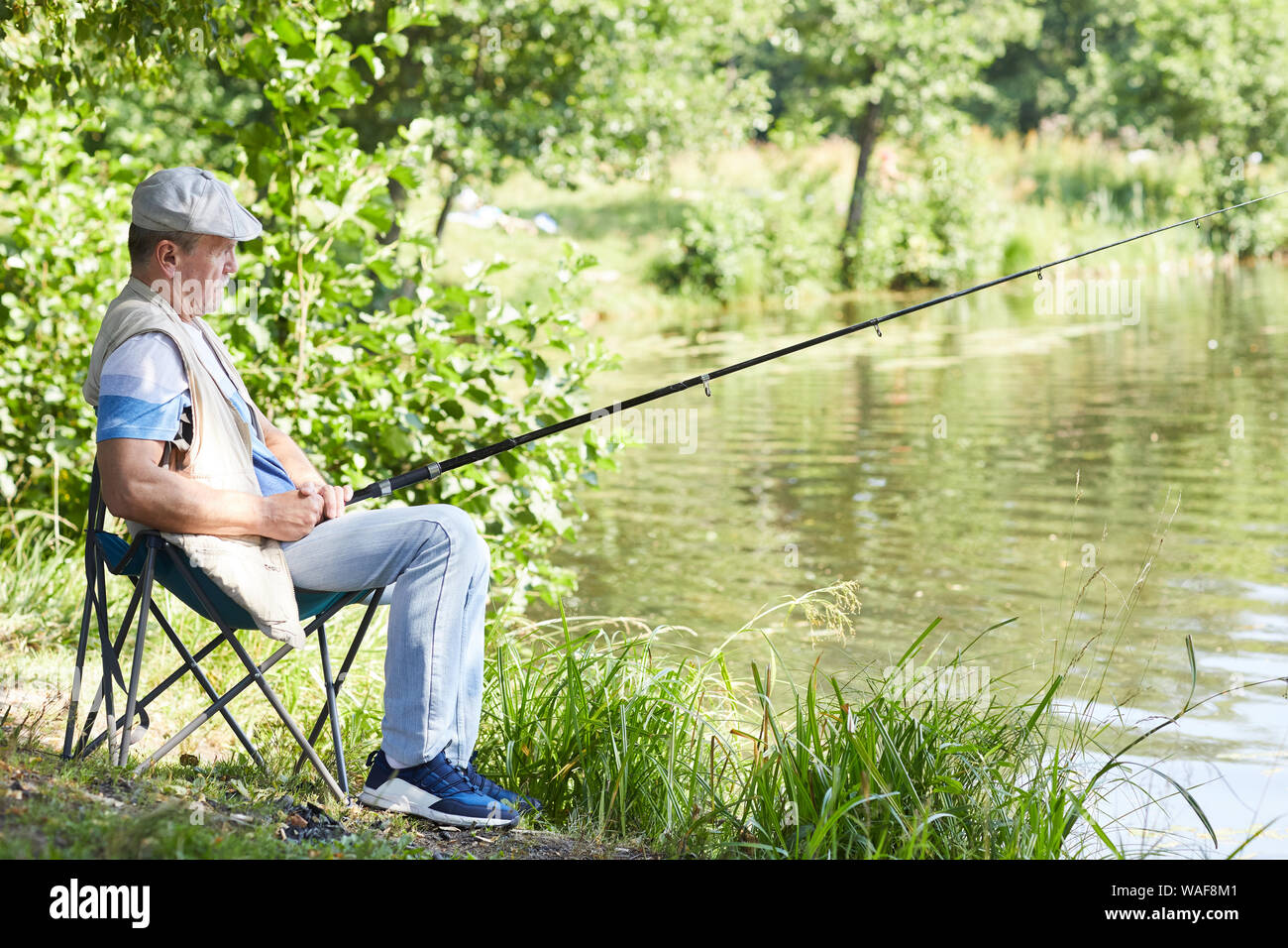 Senior man with fishing rod catching fish while sitting on chair near the  lake outdoors Stock Photo - Alamy