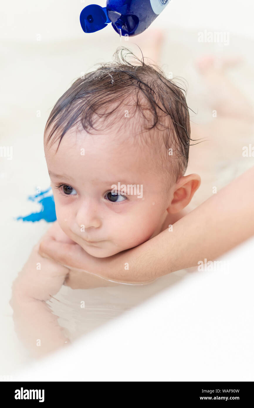 Young mother washing her baby boy's hair at bathroom. 1 year old kid