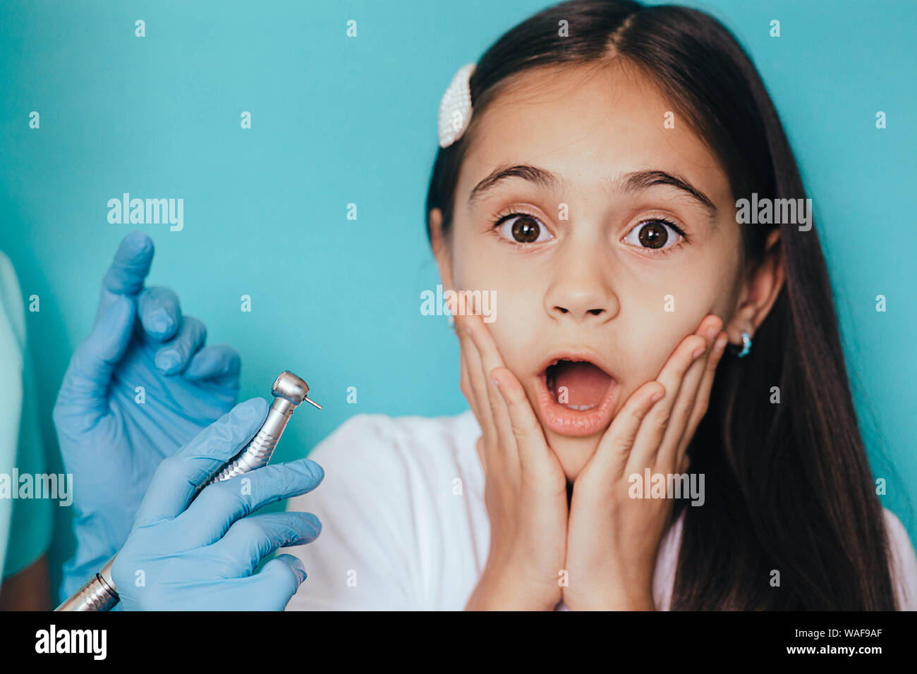 Child teeth treatment . little mixed race girl scared emotion with dental drill on blue background Stock Photo