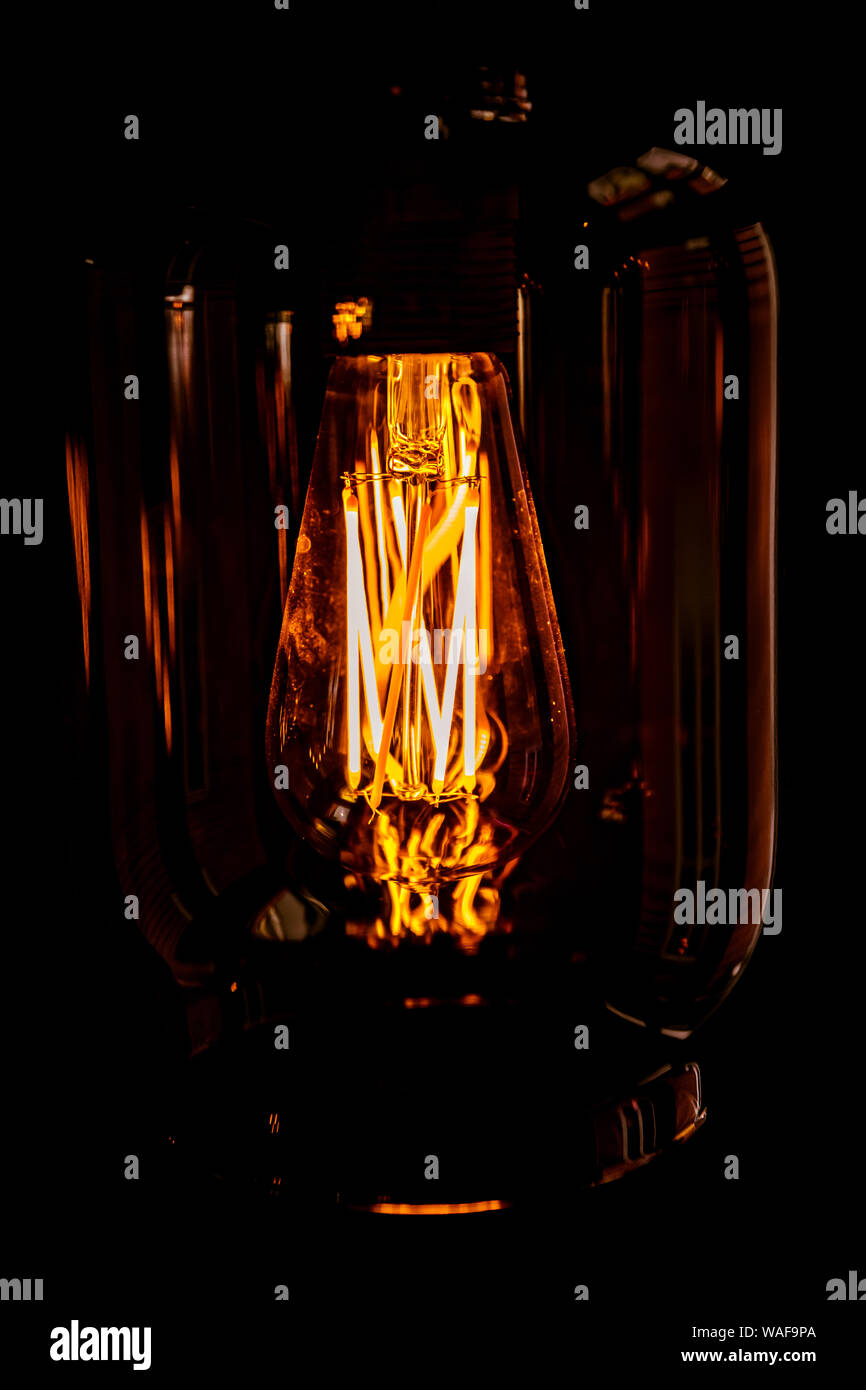 A hanging bare electric lightbulb with a glass lampshade and a warm glow. Stock Photo