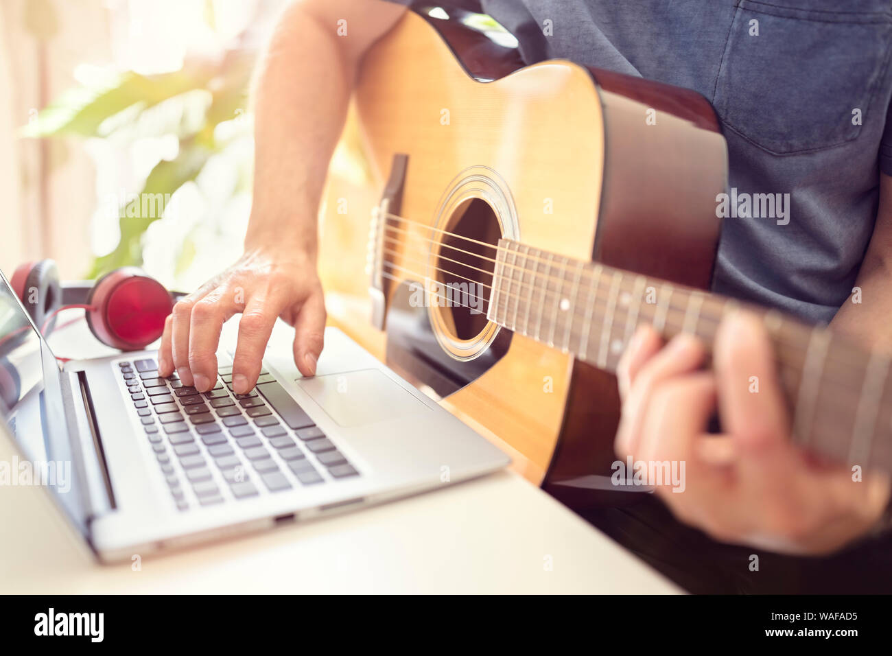 Musician playing acoustic guitar and recording music on computer or learning fom online lesson Stock Photo