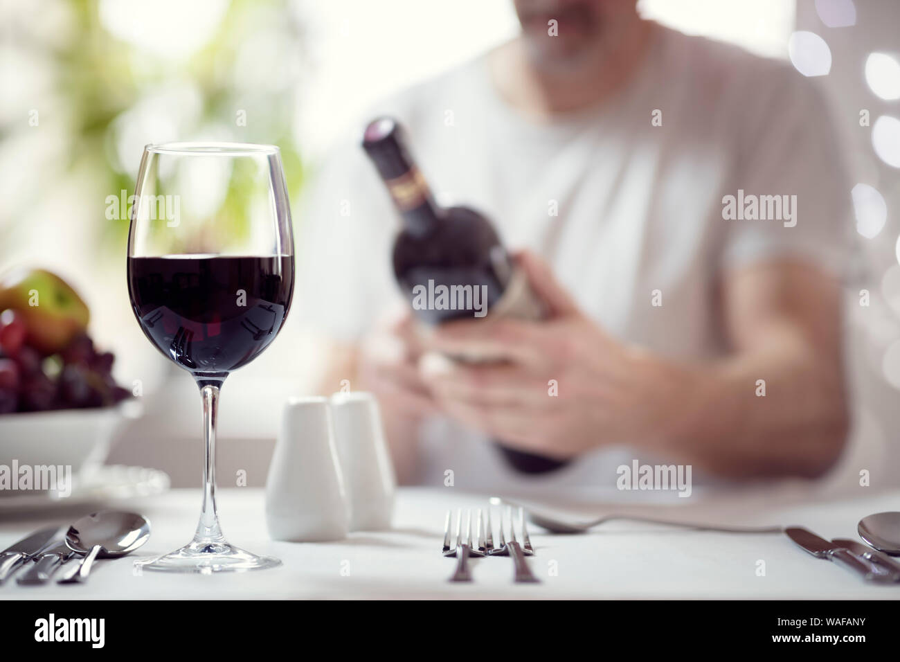 Man reading red wine bottle label in restaurant focus on glass Stock Photo
