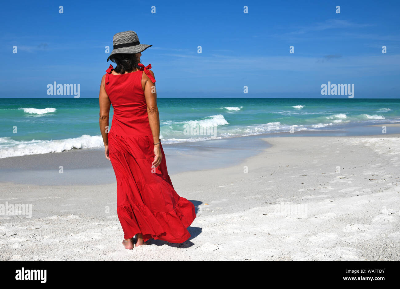 Beautiful Woman in a Red Summer Dress and Hat Standing on the Beach Stock Photo