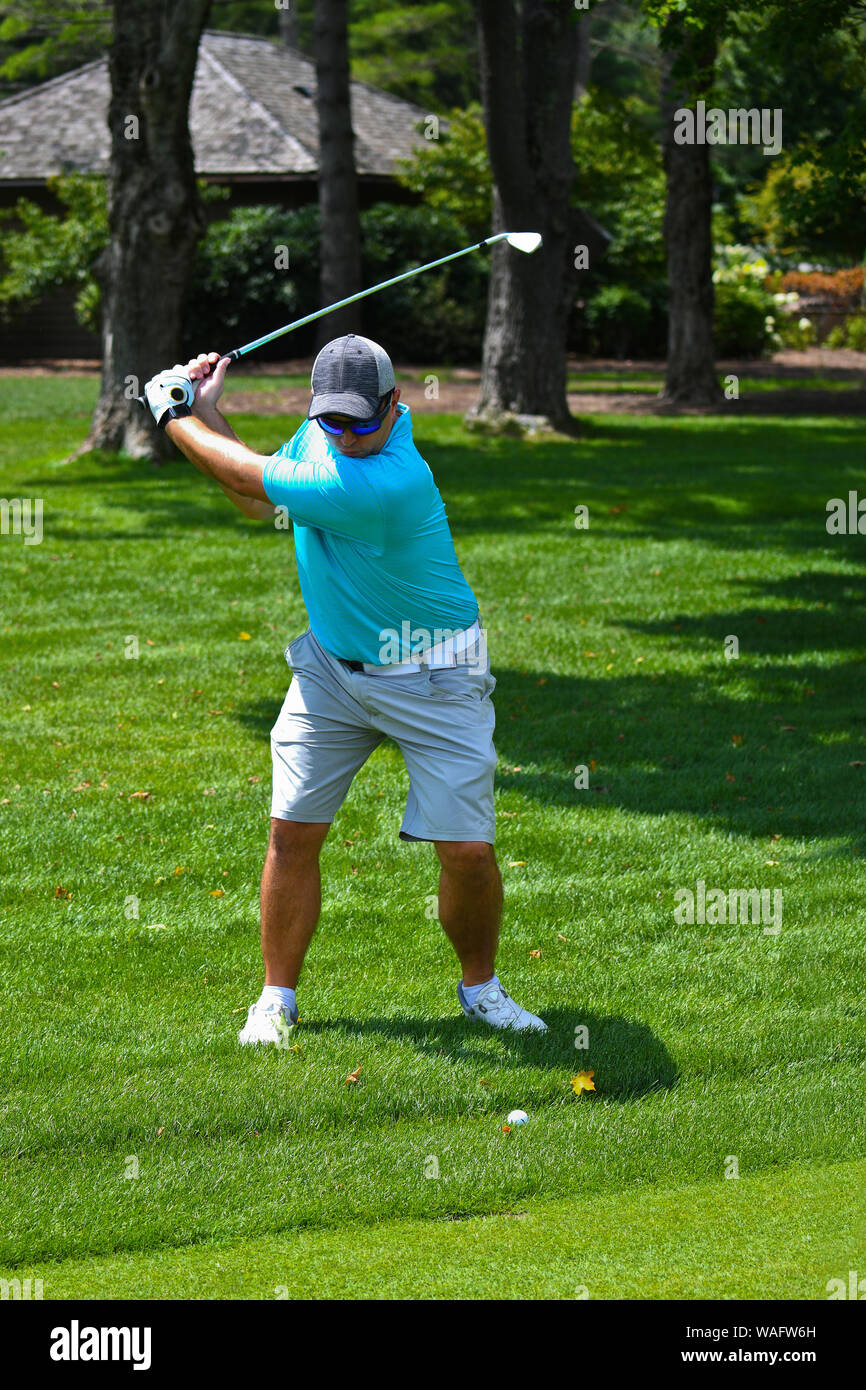 Young Man Swinging a Golf Club to Hit a Golf Ball Down the Fairway