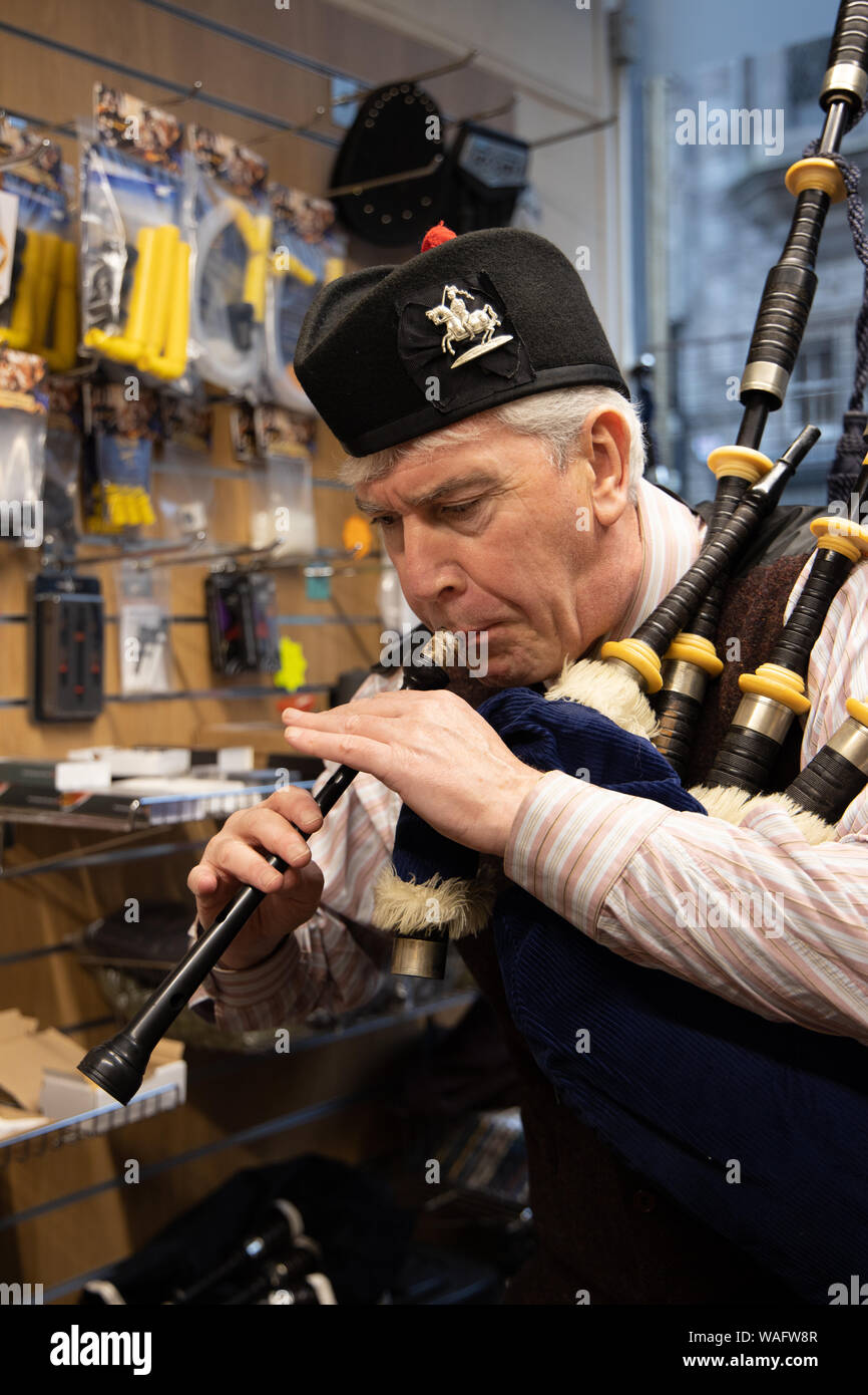 Testing the sound Edinburgh piper Alastair Wilkinson inside the old Kilberry Bagpipe shop in St Mary's Street, Edinburgh, Scotland Stock Photo