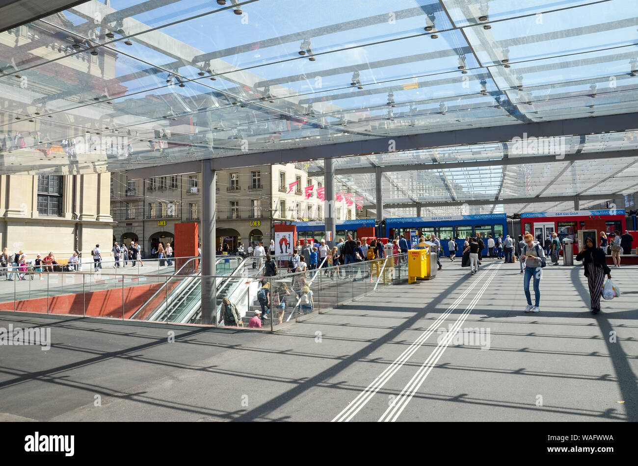 Bern, Switzerland - August 14 2019: People walking under the roof by tram station. The station is adjacent to the main train station. Tram in background. Public transport. Daily life. Swiss capital. Stock Photo