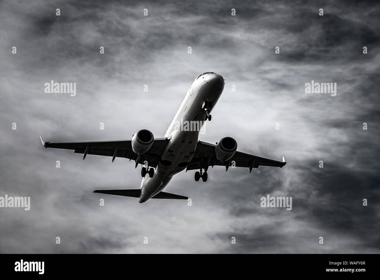 Airplane landing in front of dramatic sky in black and white Stock Photo