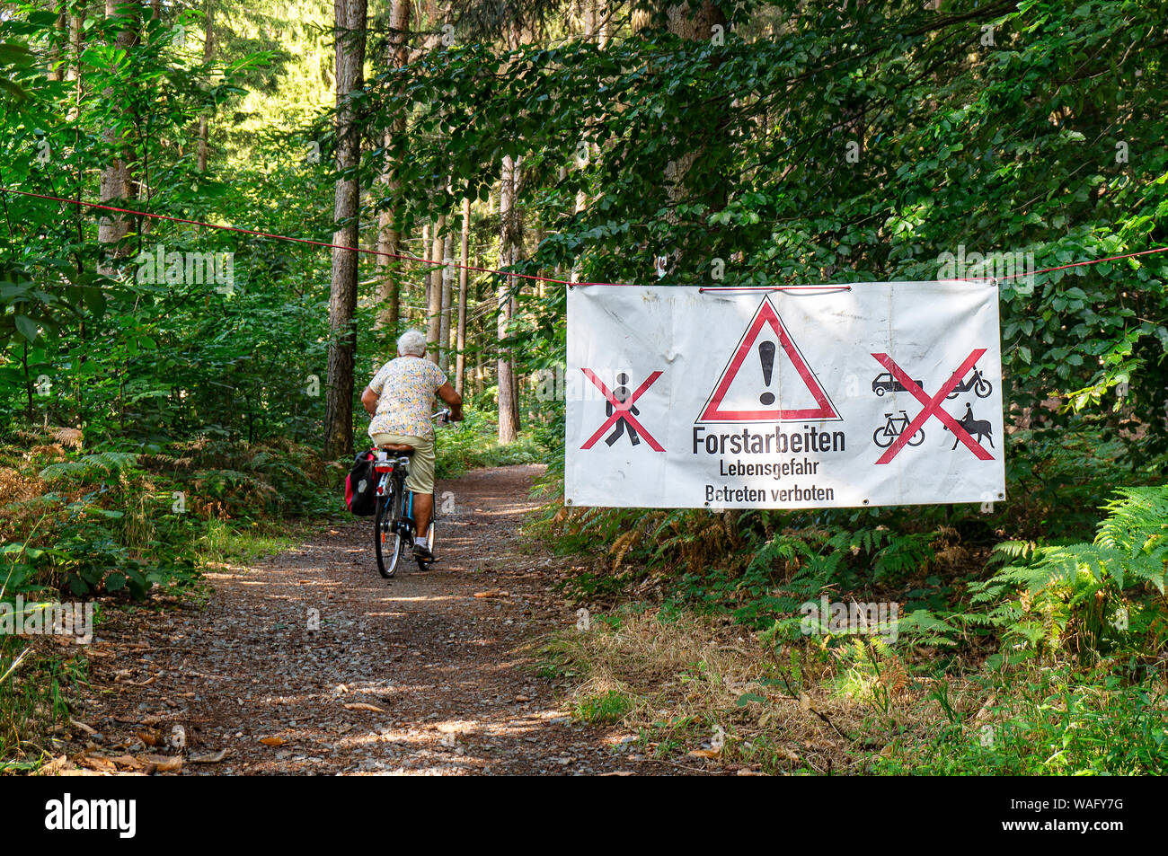 Cyclist on a forest path next to a sign for forestry work Stock Photo