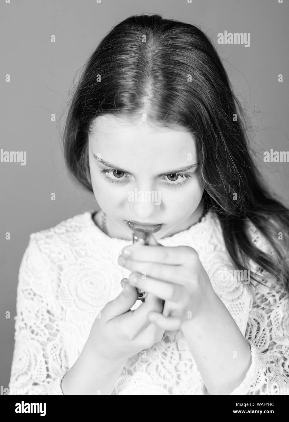 Learning colors with lipstick. Cute small little child looking at lipstick. Adorable little girl holding lipstick tube. Beauty model choosing rosy lipstick for her lips. Stock Photo