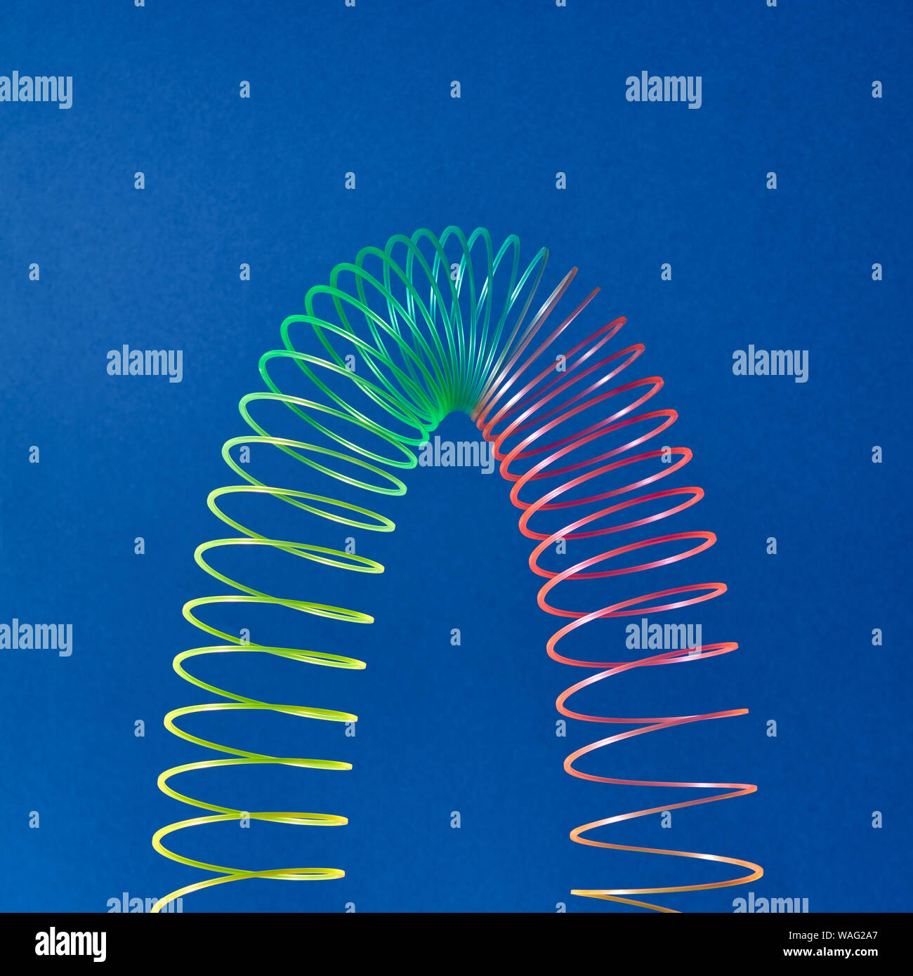 Stratching colorful toy spiral in the shape of parabola on a blue ...