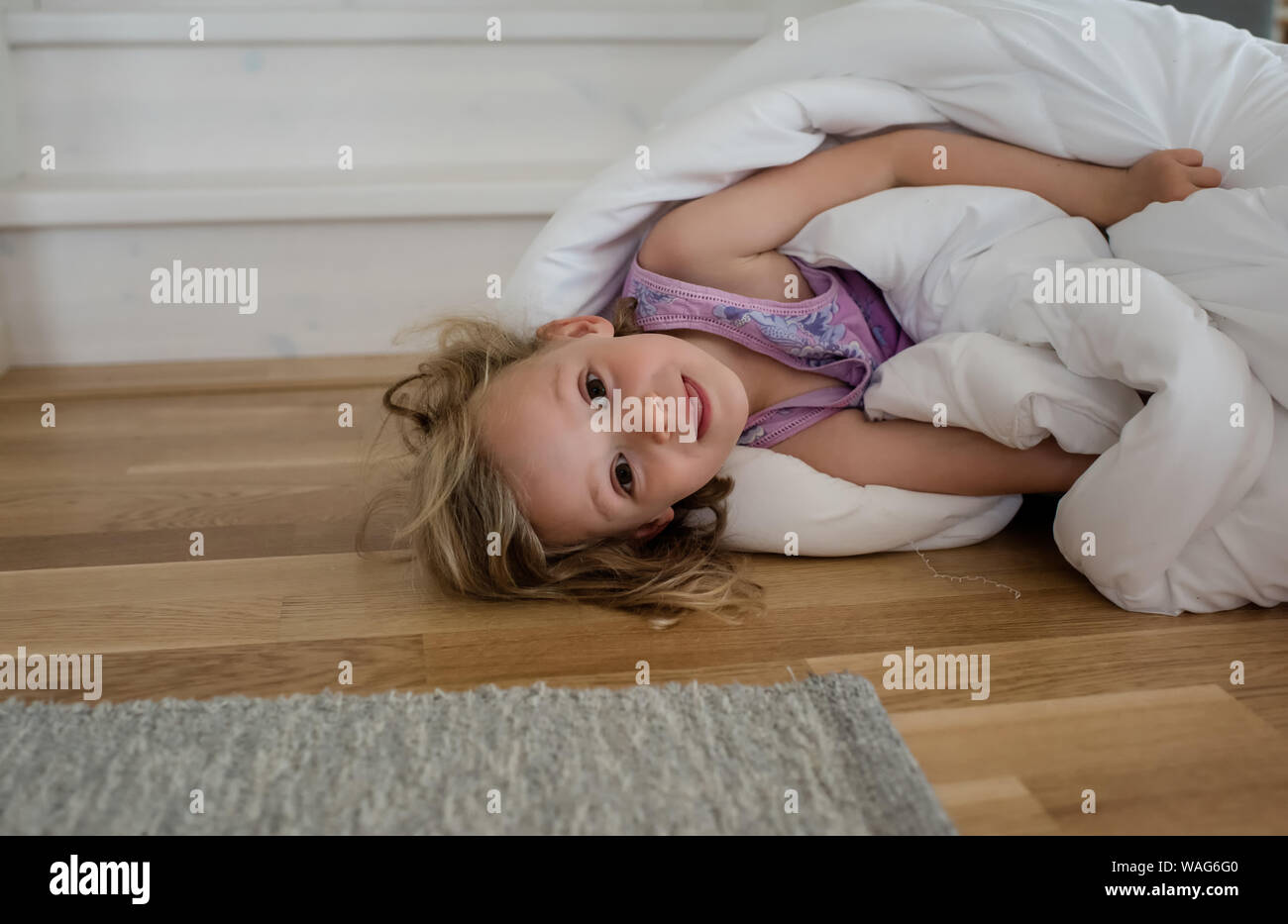 portrait of a young blond girl playing in a duvet on the floor at home Stock Photo