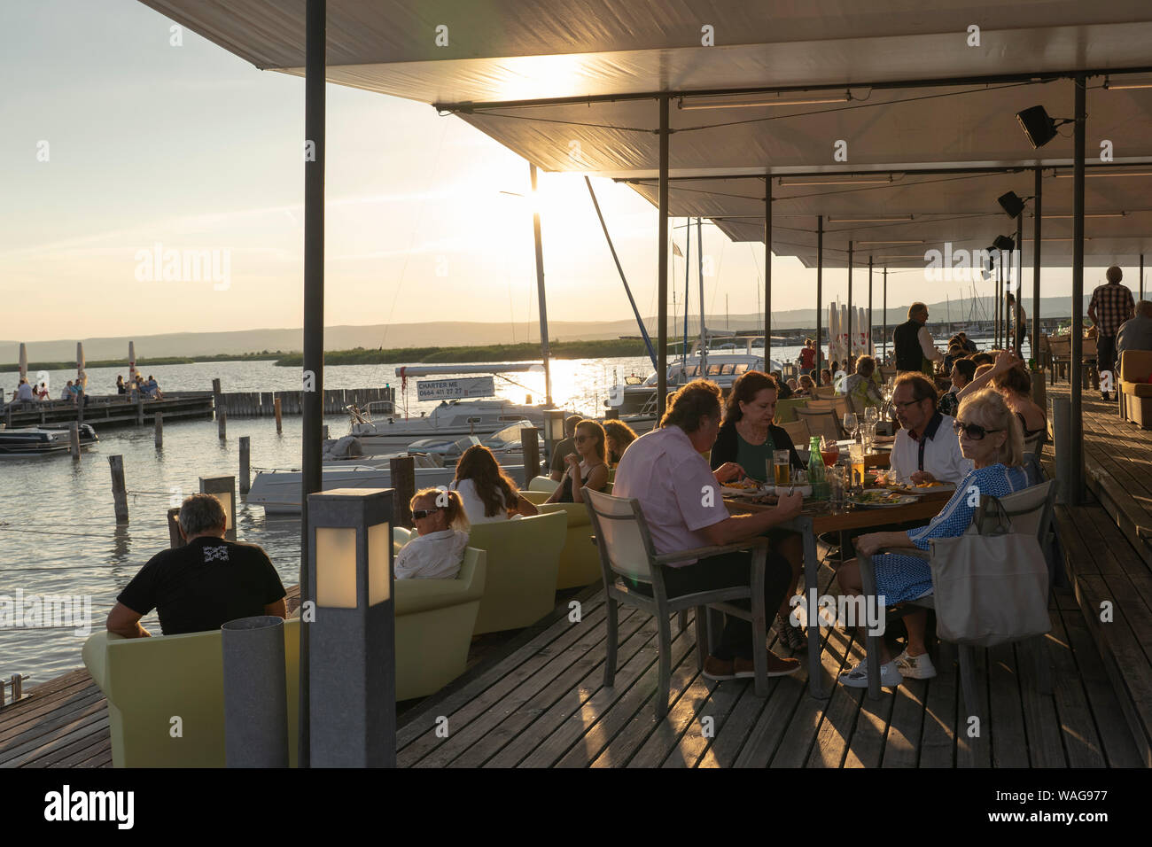 Diners at the Mole West bar and restaurant enjoying the sun setting and the views across Neusiedle See, a popular tourist destination in Burgenland Stock Photo