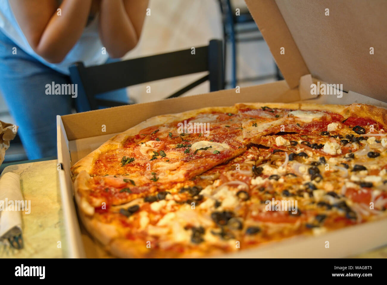 A steaming hot combination pizza in a box with an excited customer in the backgound. Stock Photo
