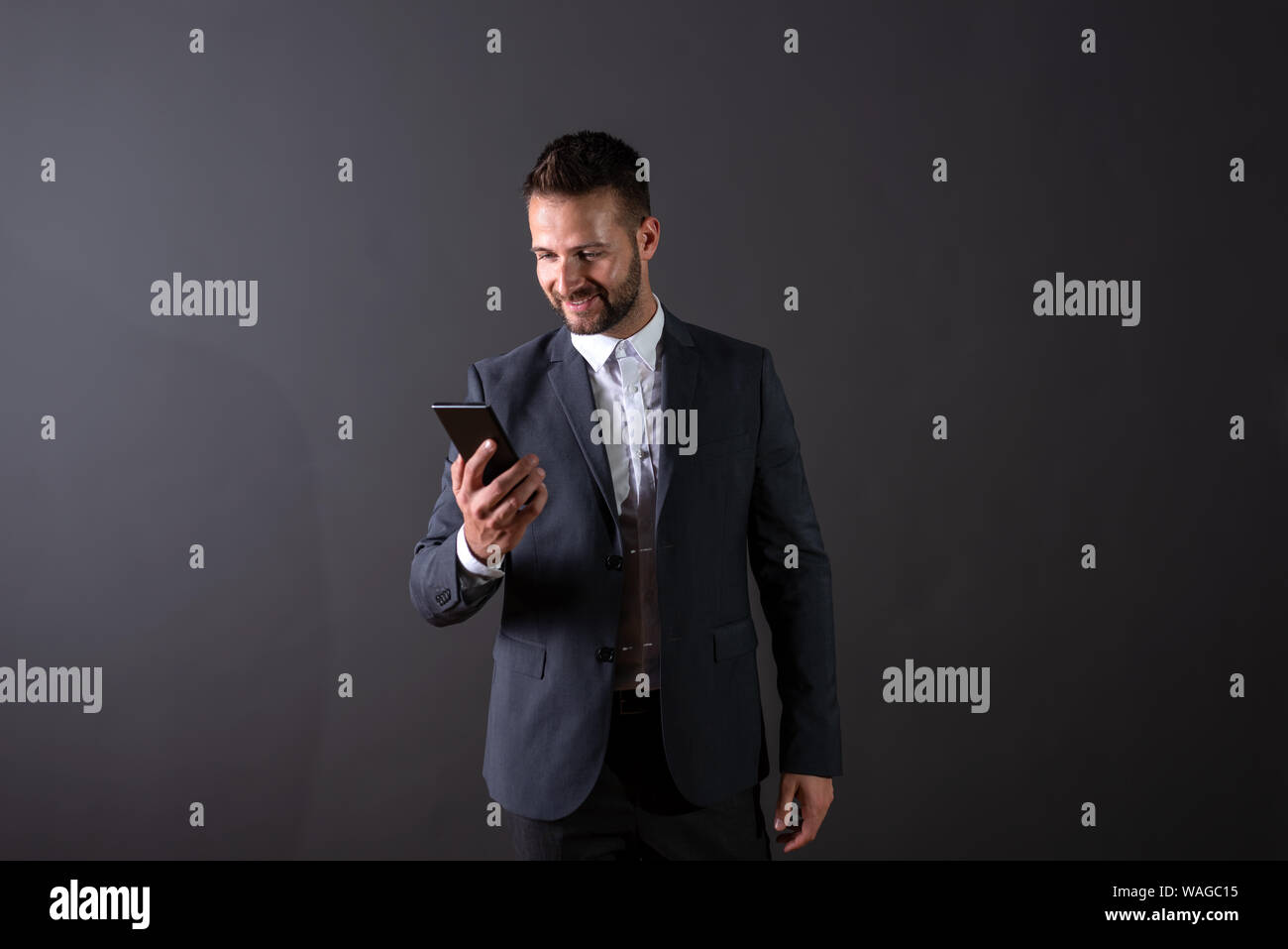 A smiling handsome young businessman in a suit using his smartphone in ...