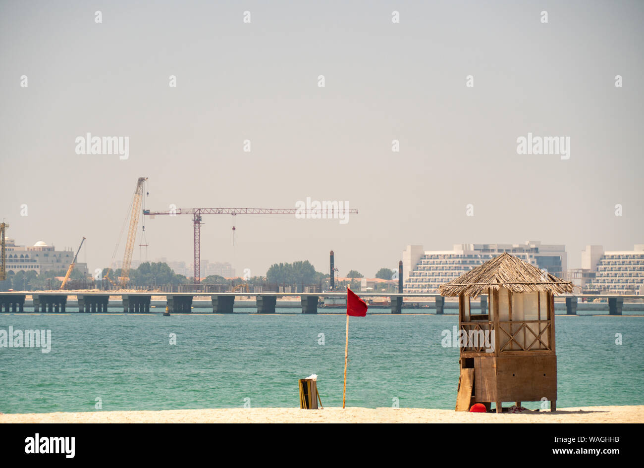 View of an empty beach with a red flag and life guard post. Dubai beach with a crane in the background Stock Photo