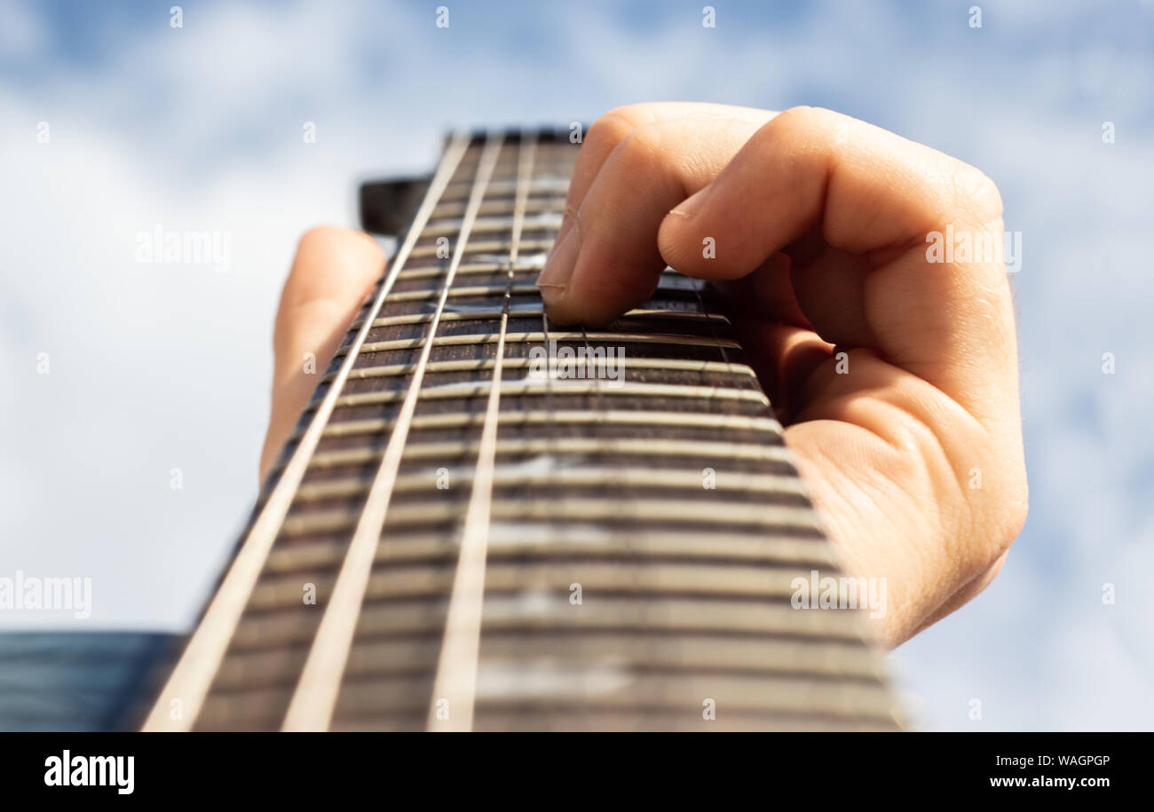 Male hand playing electric guitar and bending the strings with blue cloudy sky in the background Stock Photo
