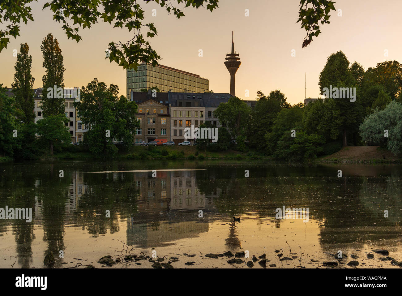 Outdoor silhouette view with twilight sky at Ständehaus park with reflection in the lake, and background of buildings and Rhine tower. Stock Photo