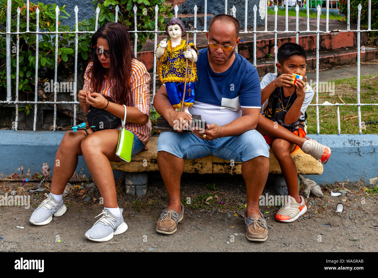 A Filipino Family Resting On A Bench During The Ati-Atihan Festival, Kalibo, Panay Island, Aklan Province, The Philippines. Stock Photo