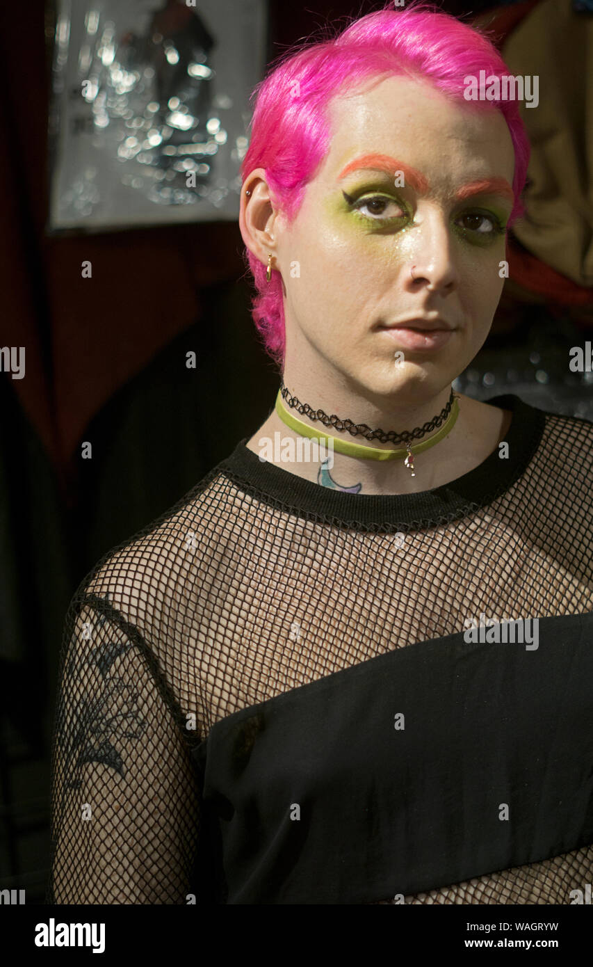 A transitioning trans woman with pink hair, orange eyebrows & green eye makeup poses for a portrait in Manhattan, New York City. Stock Photo