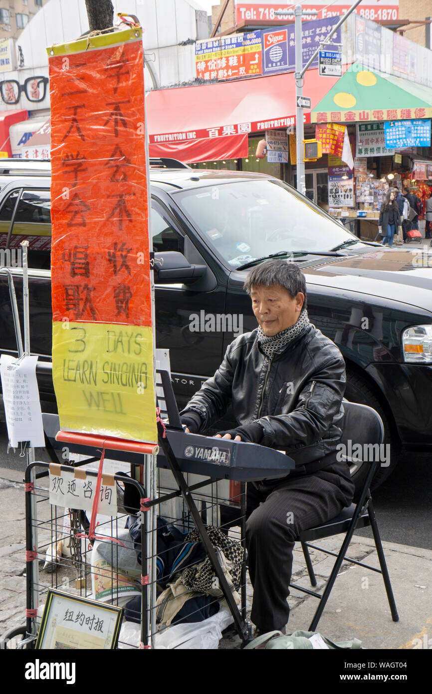A Korean man playing the piano on Main Street on a winter afternoon in Flushing, Queens, NY and advertising singing lessons. Stock Photo