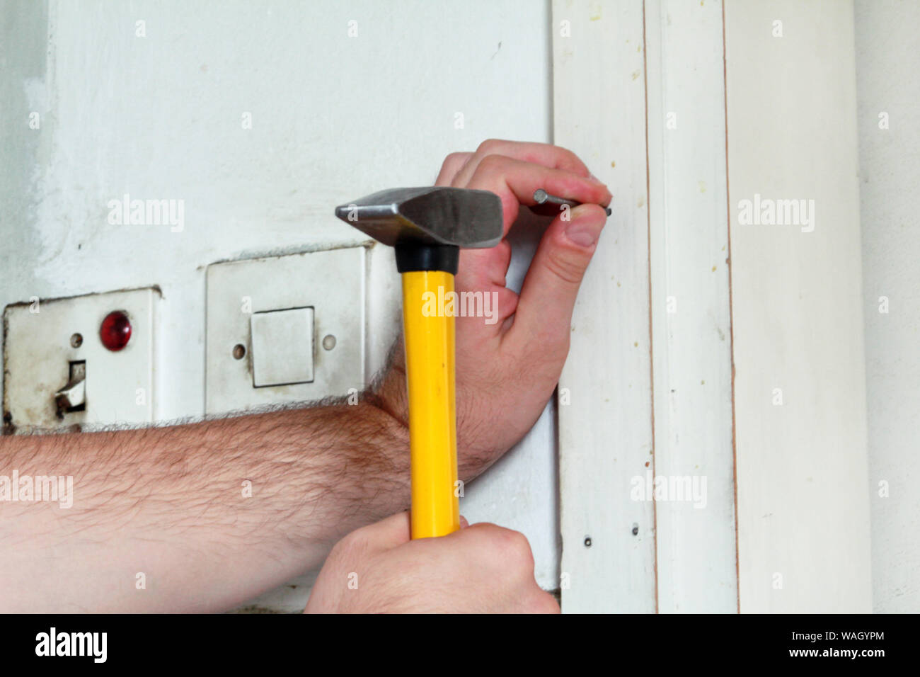 Construction worker and handyman working on renovation work. Builder with  yellow hammer strikes and nails a nail into wooden wall of kitchen door  Stock Photo - Alamy
