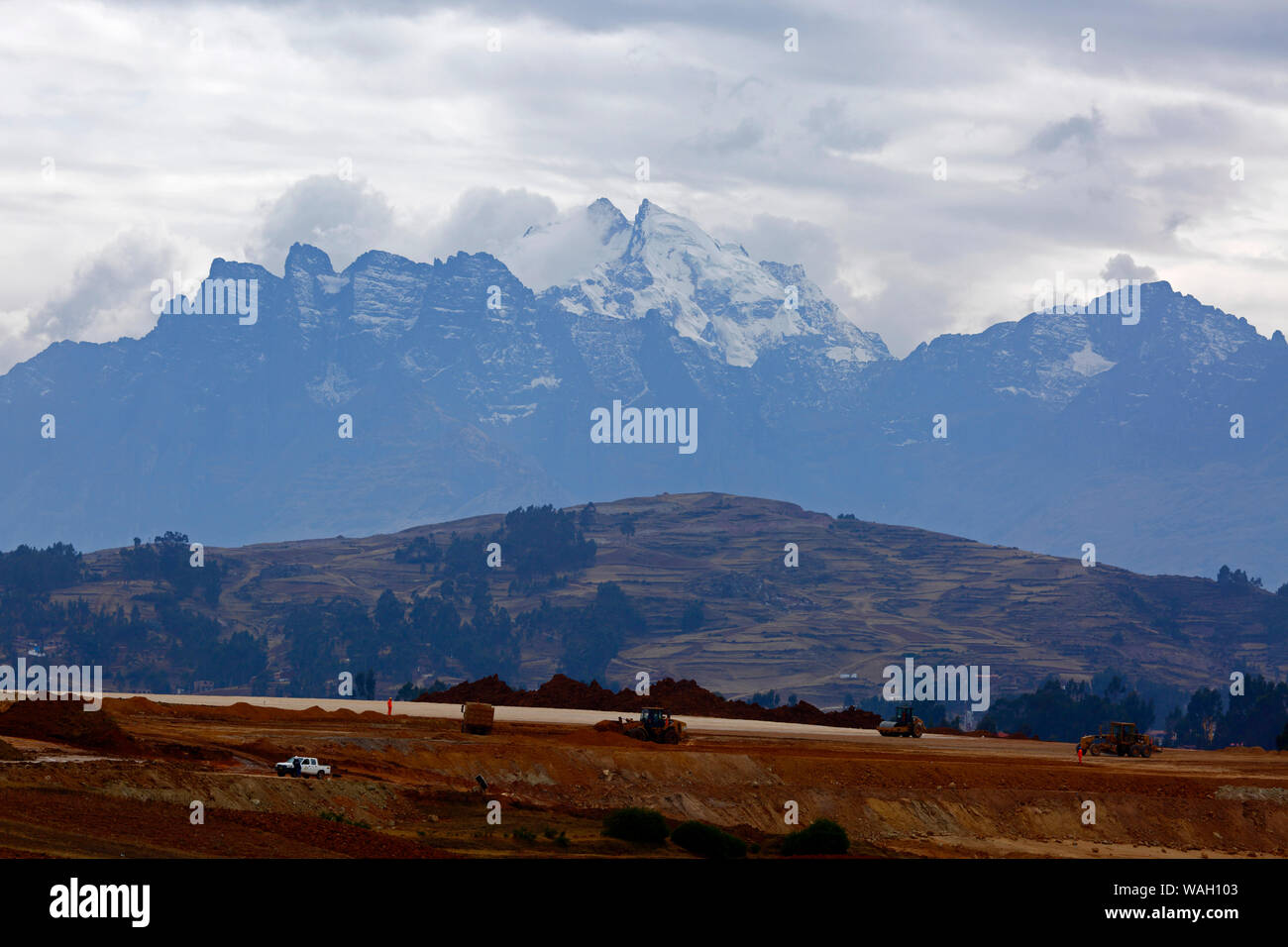 Heavy machinery working moving earth, the start of construction at the site of a new international airport at Chinchero for Cusco and Machu Picchu. In the background is Mt Sawasiray, one of the peaks of the Cordillera Urubamba mountain range. Cusco Region, Peru Stock Photo