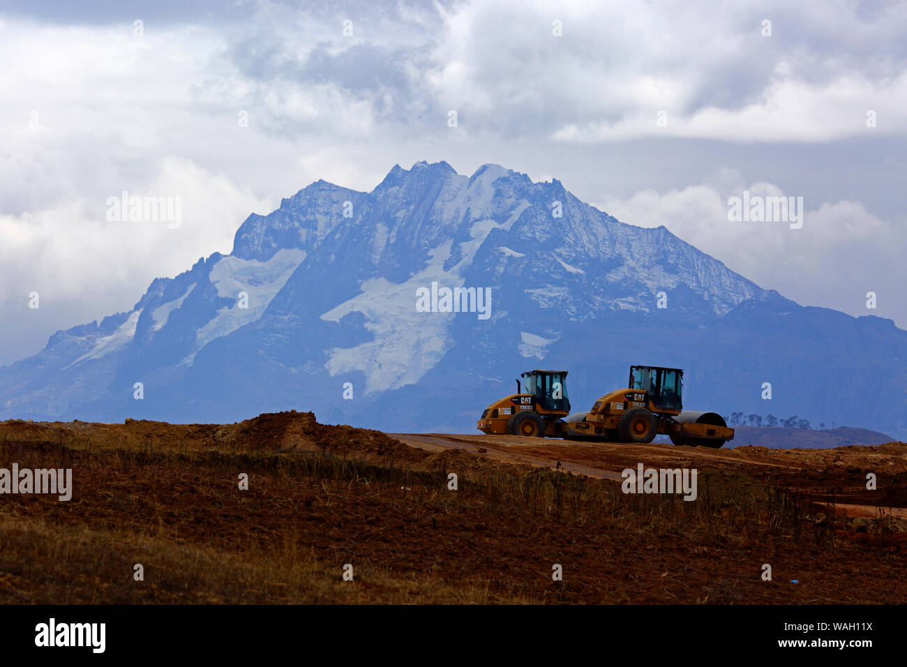 Heavy machinery working moving earth, the start of construction at the site of a new international airport at Chinchero for Cusco and Machu Picchu. In the background  is Mt Chicon, one of the peaks of the Cordillera Urubamba mountain range. Cusco Region, Peru Stock Photo