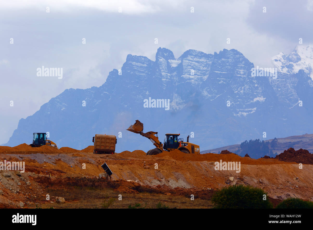 Heavy machinery working moving earth, the start of construction at the site of a new international airport at Chinchero for Cusco and Machu Picchu. In the background are the peaks of the Cordillera Urubamba mountain range. Cusco Region, Peru Stock Photo